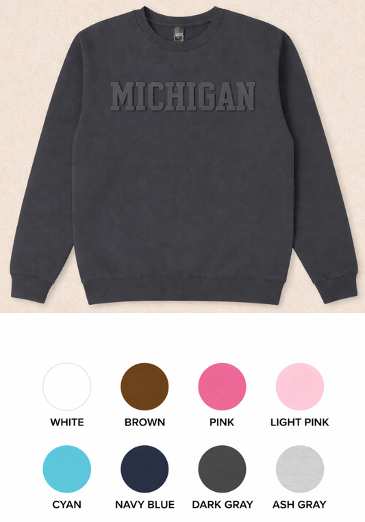 Gray sweatshirt with 'MICHIGAN' text embossed print on a beige background, color swatches below.